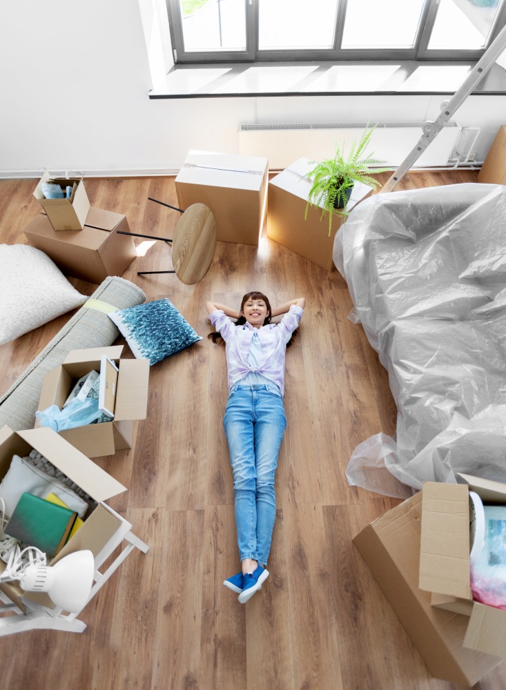 moving, people and real estate concept - happy smiling asian woman with boxes lying on floor at new home. happy woman with boxes moving to new home