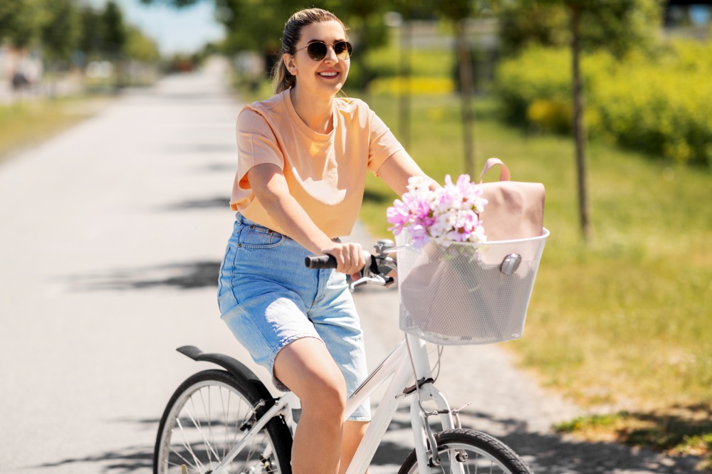 people, leisure and lifestyle - happy young woman with flowers and bag in basket of bicycle on city street. woman with flowers in bicycle basket in city