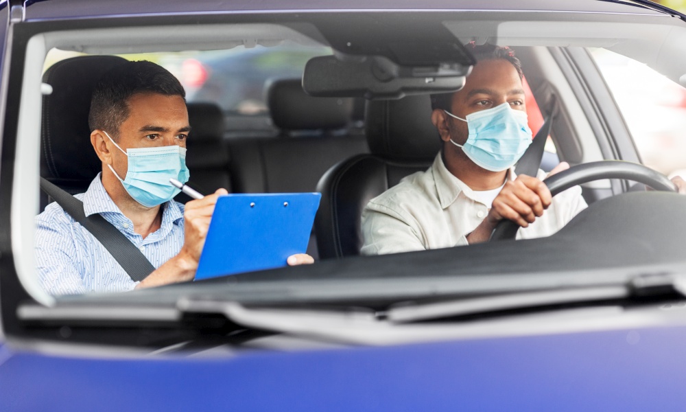 driver courses, health and people concept - young man and driving school instructor in mask with clipboard in car. car driving school instructor and driver in mask
