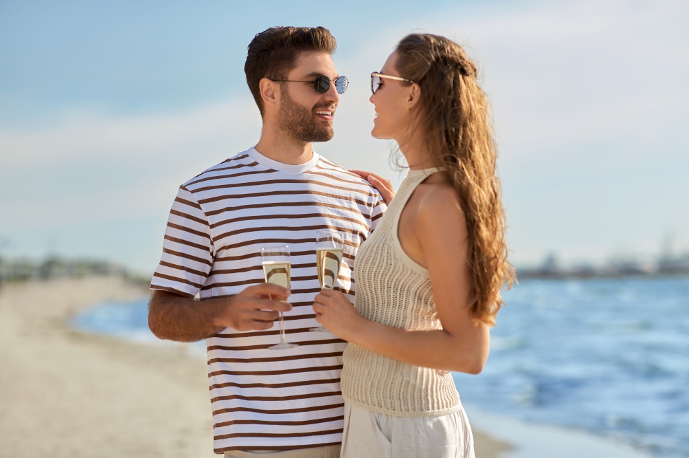leisure, relationships and people concept - happy couple in sunglasses drinking champagne on summer beach. happy couple drinking champagne on summer beach