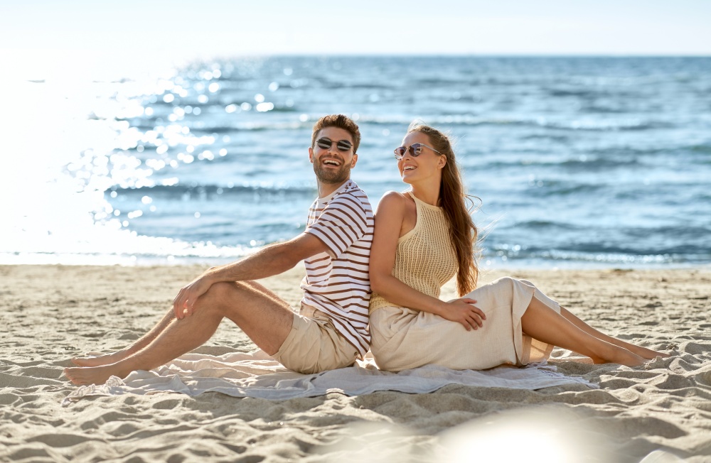 leisure, relationships and people concept - happy couple in sunglasses sitting back to back on summer beach. happy couple sitting back to back on summer beach