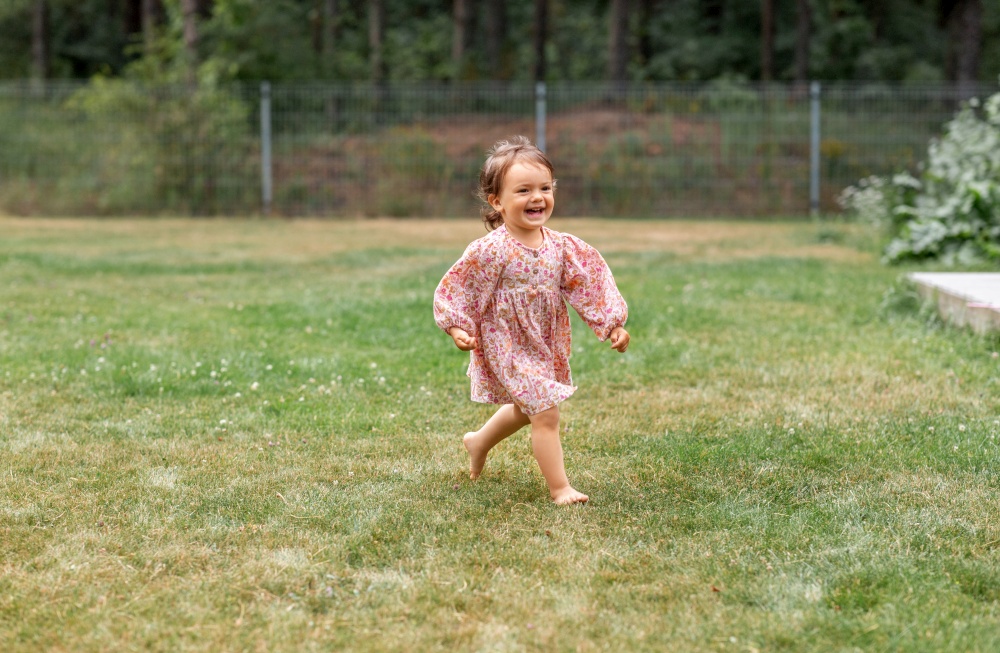 childhood, leisure and people concept - happy little baby girl running barefoot on grass. happy little baby girl running barefoot on grass