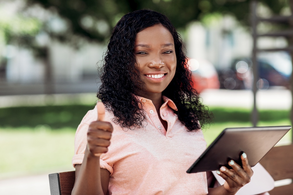 technology, lifestyle and people concept - happy smiling african american woman with tablet pc computer in city showing thumbs up. african american woman with tablet pc in city