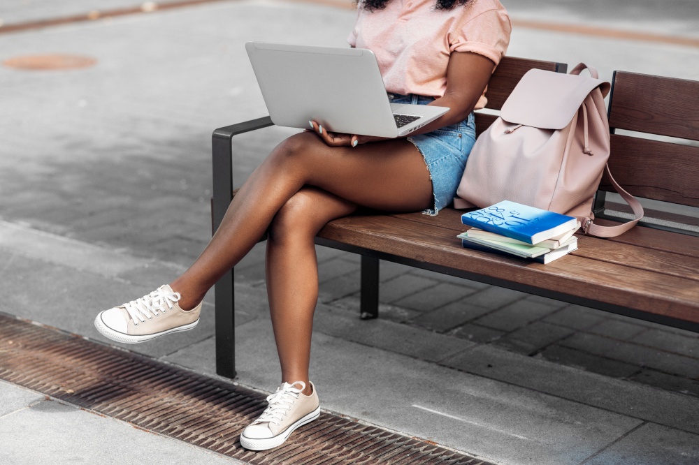 technology, education and people concept - african american student girl with laptop computer and books in city. african student girl with laptop and books in city