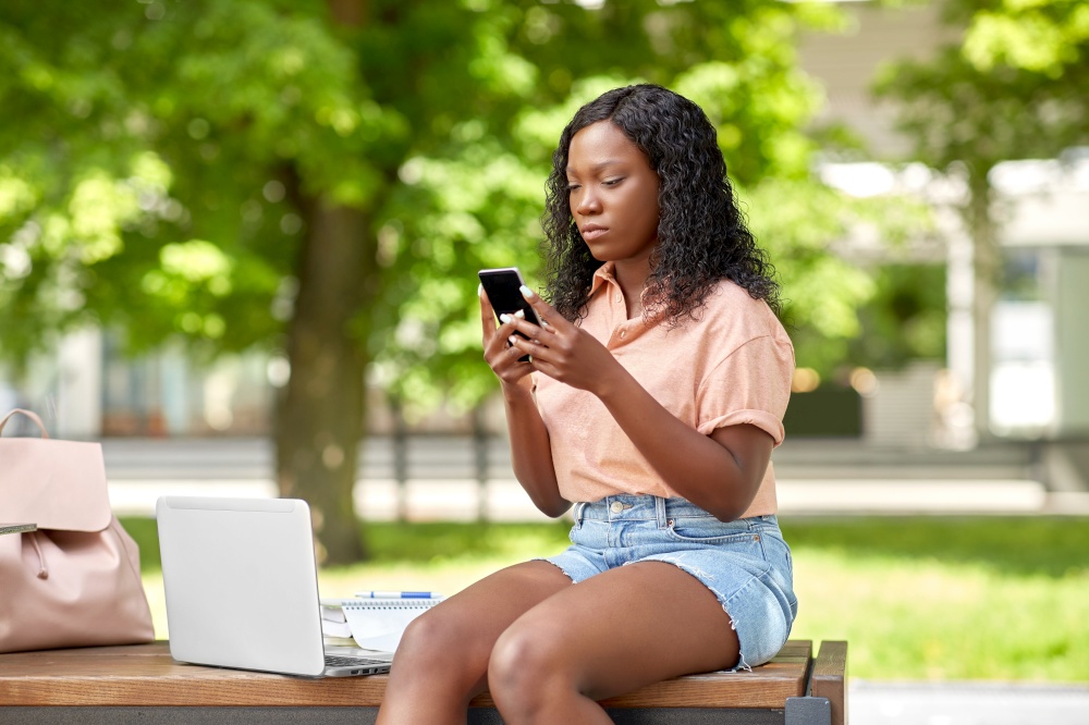 technology, education and people concept - african american student girl with smartphone and laptop computer in city. african student girl with laptop and smartphone