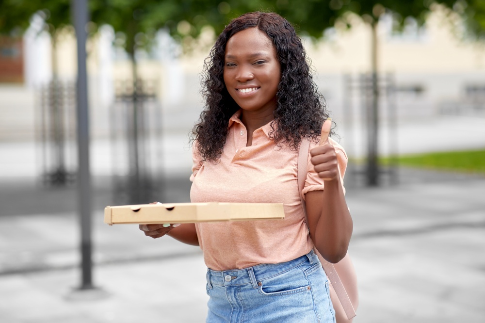 education, school and people concept - happy smiling african american student girl with takeaway pizza box on city street showing thumbs up. african student girl with pizza showing thumbs up