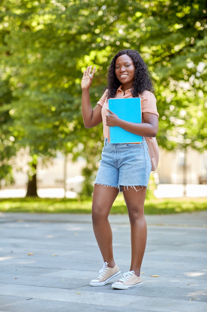 education, school and people concept - happy smiling african american student girl with notebooks in city waving hand. african student girl with notebooks in city