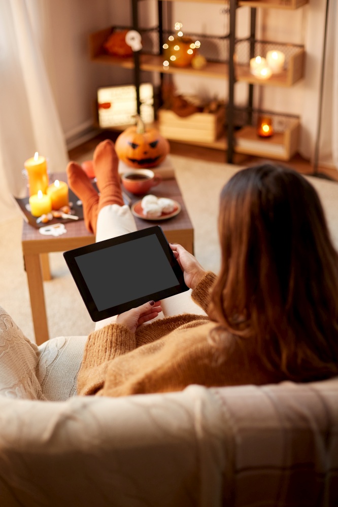 halloween, holidays and leisure concept - young woman with tablet pc computer at home. woman with tablet pc at home on halloween
