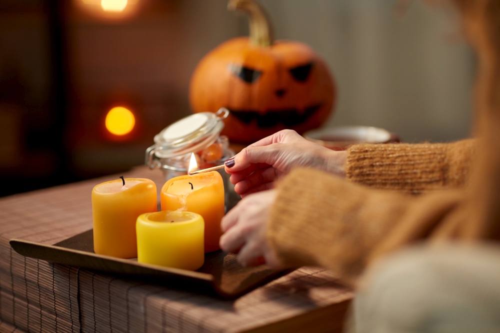 holidays and leisure concept - woman&rsquo;s hand with match lighting candle at home on halloween. hand with match lighting candle on halloween