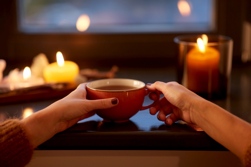 drinks, seasons and leisure concept - close up of woman&rsquo;s hands with cup of tea on window sill in autumn. hands with cup of tea on window sill in autumn