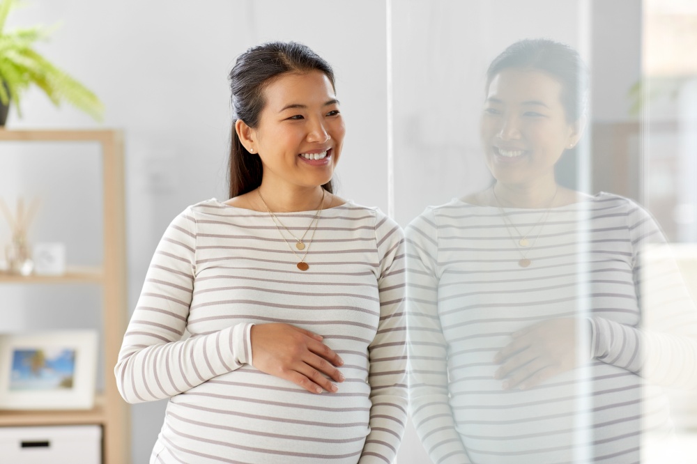 pregnancy, rest, people and expectation concept - happy smiling pregnant asian woman touching her belly at home. happy pregnant asian woman at home