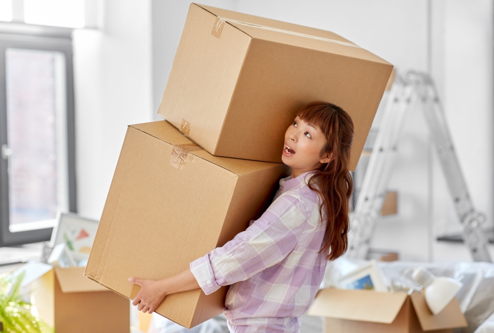 moving, people and real estate concept - asian woman holding big heavy boxes with stuff at new home. woman holding heavy boxes and moving to new home