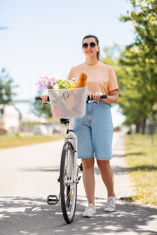 people, leisure and lifestyle - happy young woman with food and flowers in basket of bicycle walking on city street. woman with food and flowers in bicycle basket
