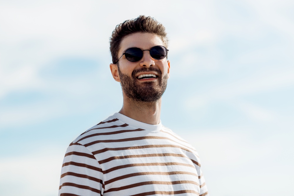 summer holidays and people concept - portrait of happy smiling young man in sunglasses over sky. smiling young man in sunglasses over sky