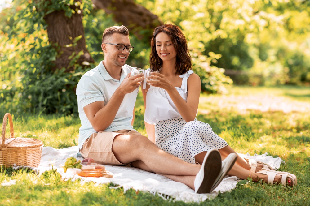 leisure and people concept - happy couple with drinks and food having picnic at summer park. happy couple having picnic at summer park