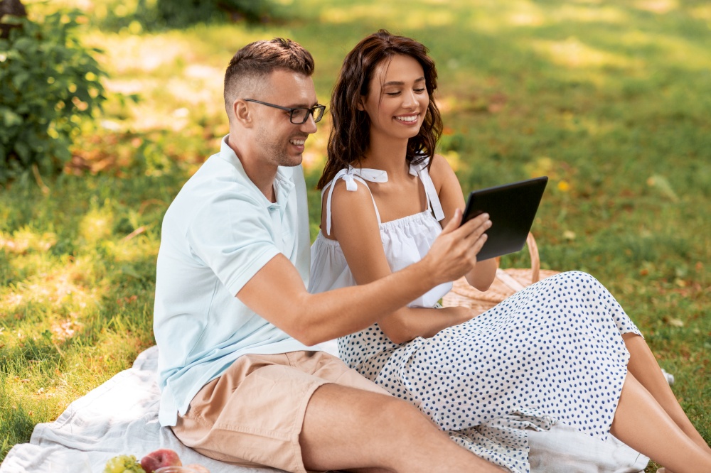 leisure and people concept - happy couple with tablet pc computer having picnic at summer park. happy couple with tablet pc at picnic in park