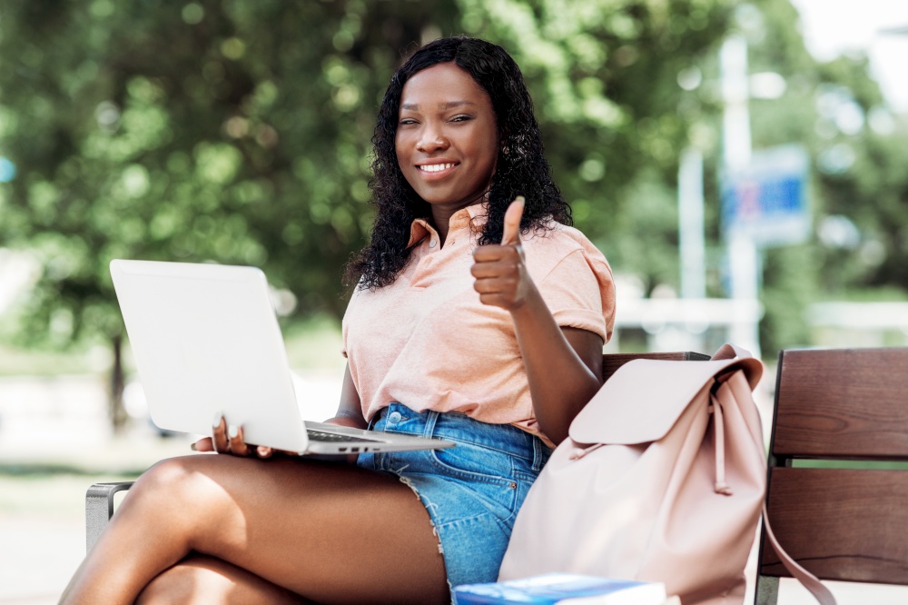 technology, education and people concept - happy smiling african american student girl with laptop computer and books in city showing thumbs up. african student girl with laptop showing thumbs up