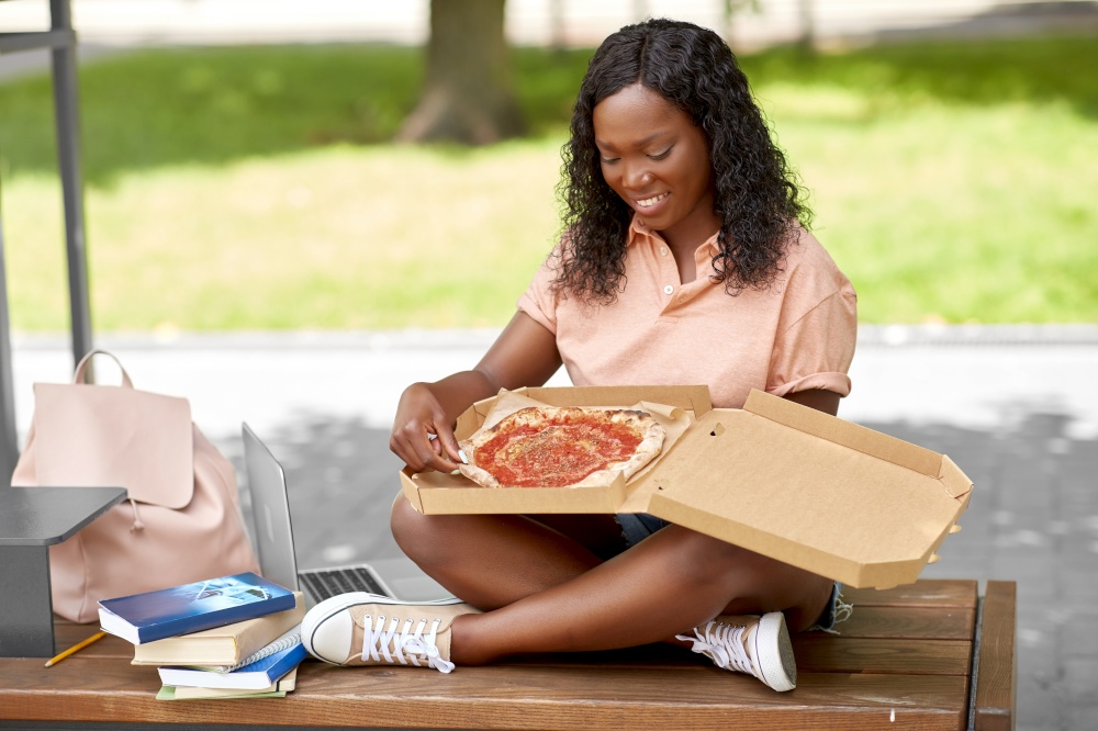 unhealthy eating, education and people concept - happy smiling african american student girl eating takeaway pizza on city street. african student girl eating takeaway pizza in city