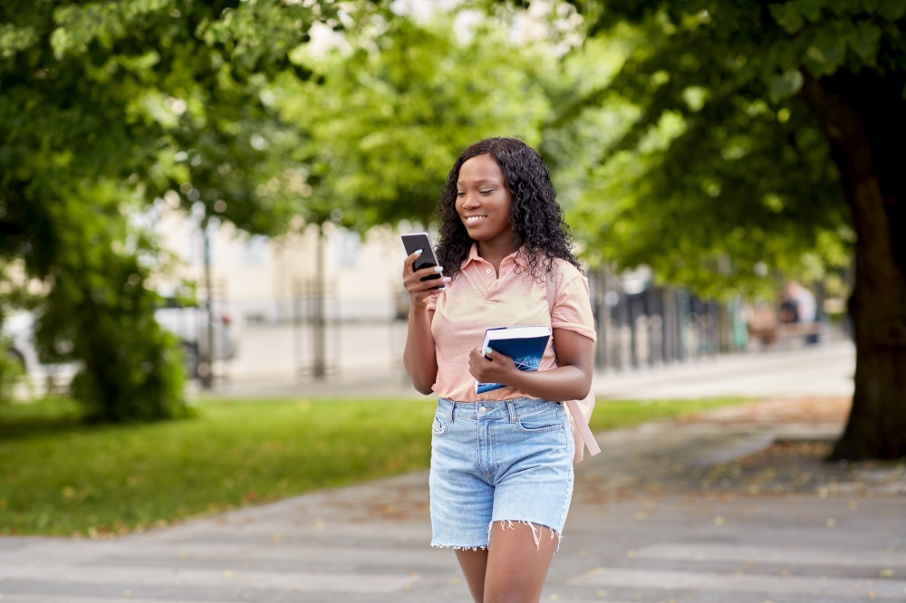 technology, education and people concept - happy smiling african american student girl with smartphone and book in city. african student girl with smartphone in city