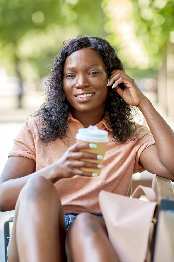 education, school and people concept - happy smiling african american student girl with takeaway coffee cup and backpack resting on bench in city. african woman with coffee and backpack in city