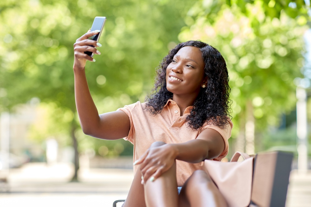 education, school and people concept - happy smiling african american student girl taking selfie with smartphone sitting on bench in city. african student girl taking selfie with smartphone