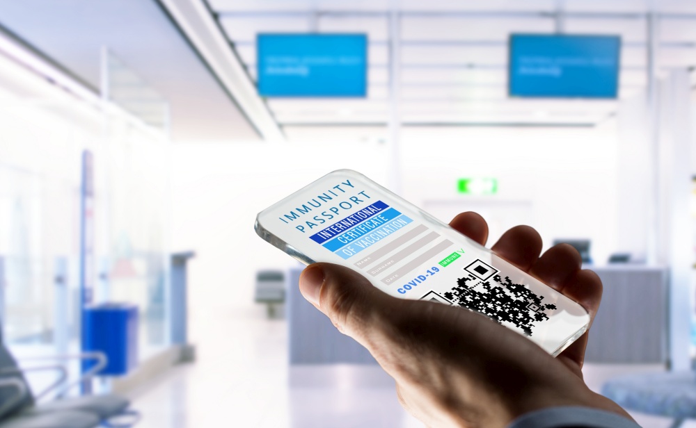 coronavirus, technology and health concept - close up of man&rsquo;s hand holding smartphone with international certificate of covid-19 vaccination on screen over airport lounge background. hand holding phone with certificate of vaccination