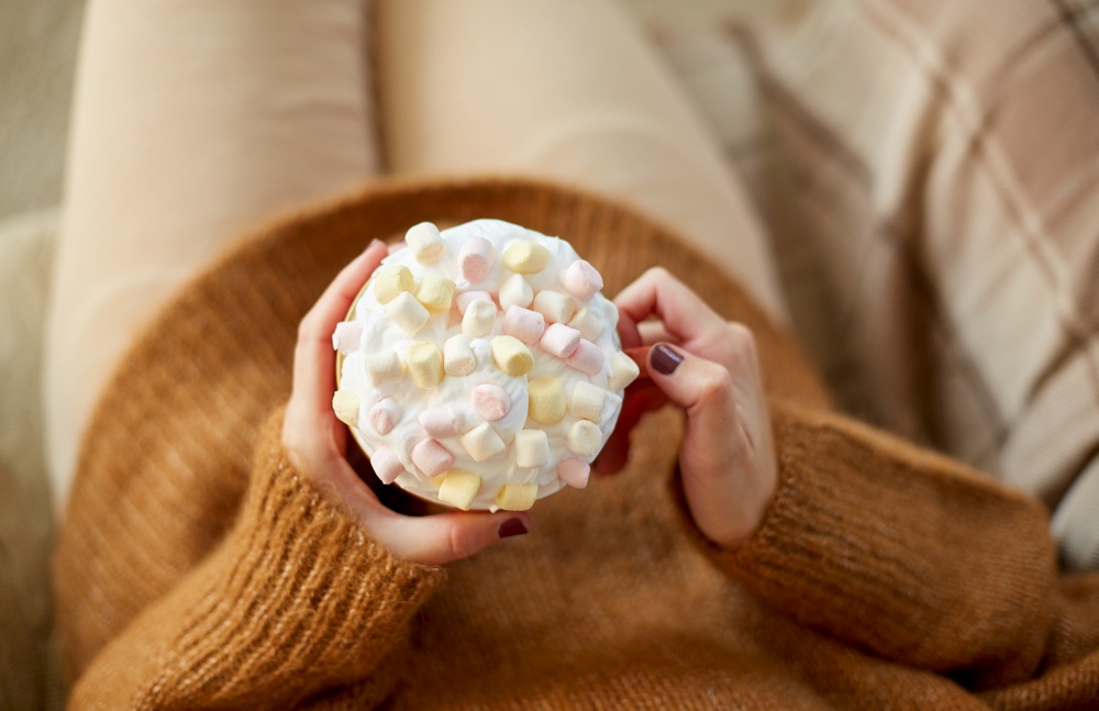 food and leisure concept - close up of woman holding mug of marshmallow and whipped cream. woman holding mug of marshmallow and whipped cream