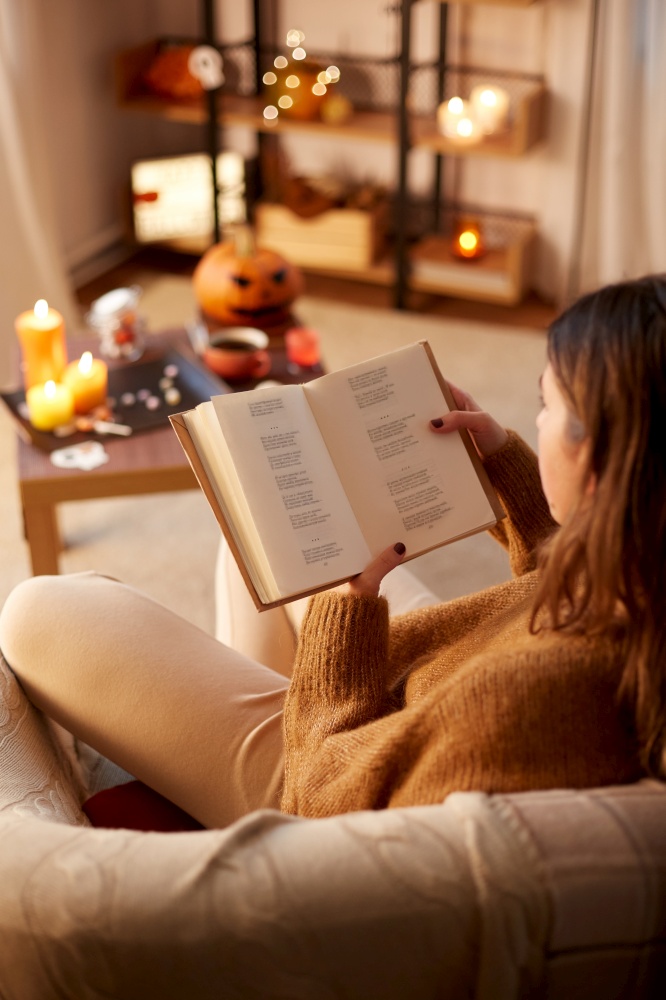halloween, holidays and leisure concept - young woman reading book at cozy home. young woman reading book at home on halloween