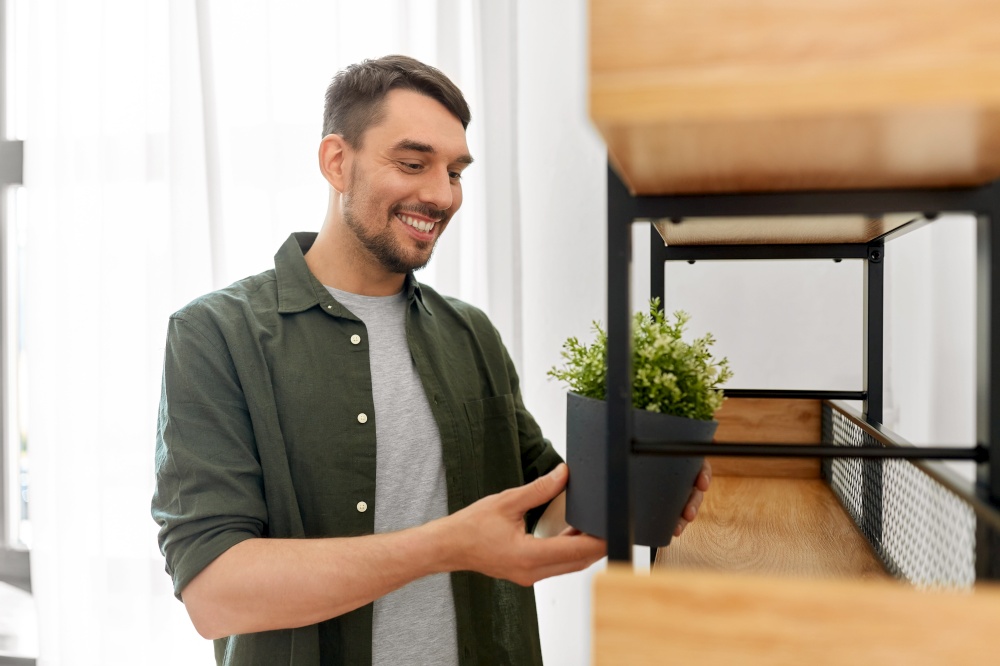 home improvement, decoration and people concept - happy smiling man placing flower in pot or houseplant to shelf. man decorating home with flower or houseplant