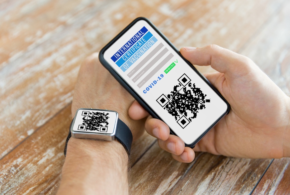 technology and health care concept - hands holding smartphone with international certificate of vaccination on screen and wearing smart watch with qr code. hands with virtual immunity passport on smartphone