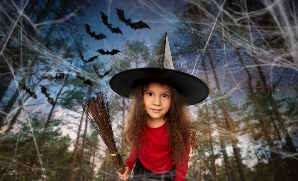 halloween, holiday and childhood concept - girl in costume and witch hat with broom over bats flying in dark night forest background. girl in black witch hat with broom on halloween