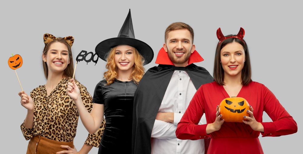 holiday, theme party and people concept - happy smiling friends in halloween costumes over grey background. happy smiling friends in halloween costumes
