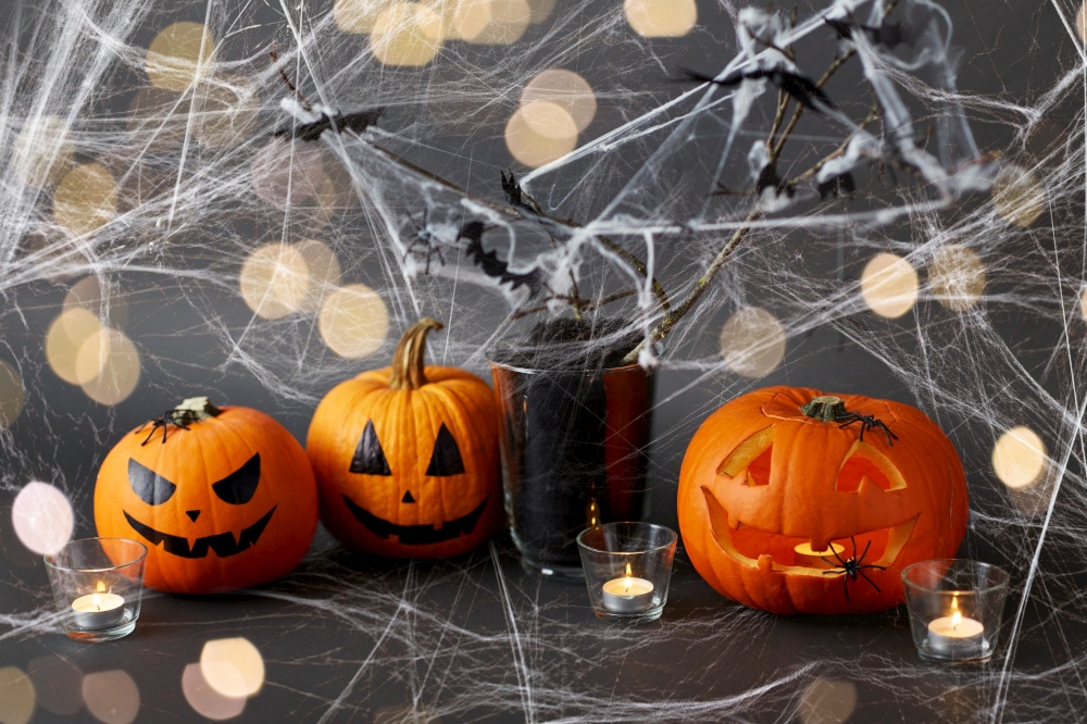 halloween and holiday concept - jack-o-lantern or carved pumpkin, burning candles and spider web decoration over spiderweb and lights. pumpkins, candles and halloween decorations