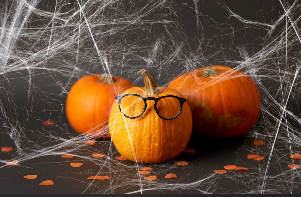 halloween and holiday concept - halloween pumpkins with glasses and spiderweb over dark background. halloween pumpkins with glasses and spiderweb
