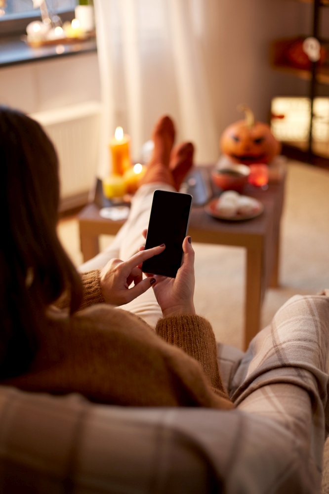 halloween, holidays and leisure concept - young woman using smartphone at home. woman using smartphone at home on halloween