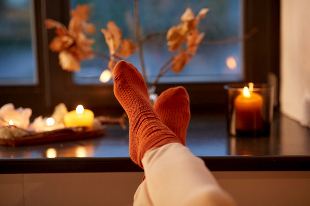 halloween, hygge and leisure concept - feet in socks on window sill at home in autumn. feet in socks on window sill at home in autumn