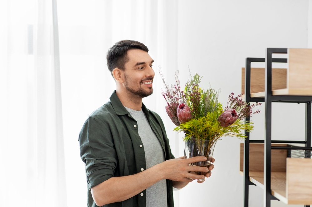 home improvement, decoration and people concept - happy smiling man placing flower in vase or houseplant to shelf. man decorating home with flower or houseplant