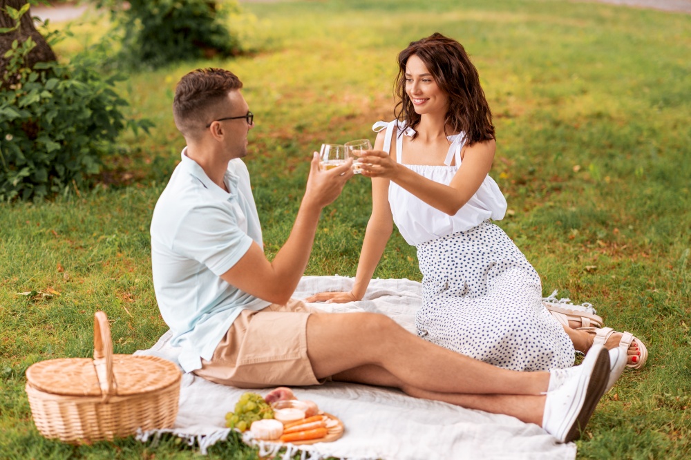 leisure and people concept - happy couple with drinks and food having picnic at summer park. happy couple having picnic at summer park