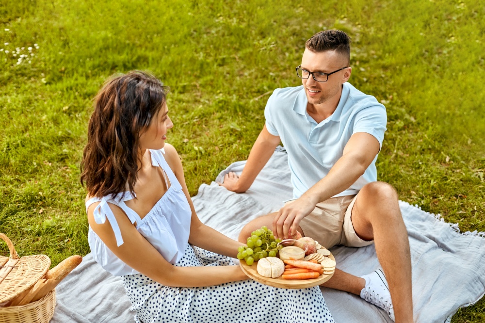 leisure and people concept - happy couple with food having picnic at summer park. happy couple having picnic at summer park