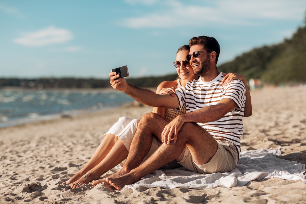 technology, leisure and people concept - happy couple taking selfie by smartphone on summer beach. happy couple taking selfie by smartphone on beach