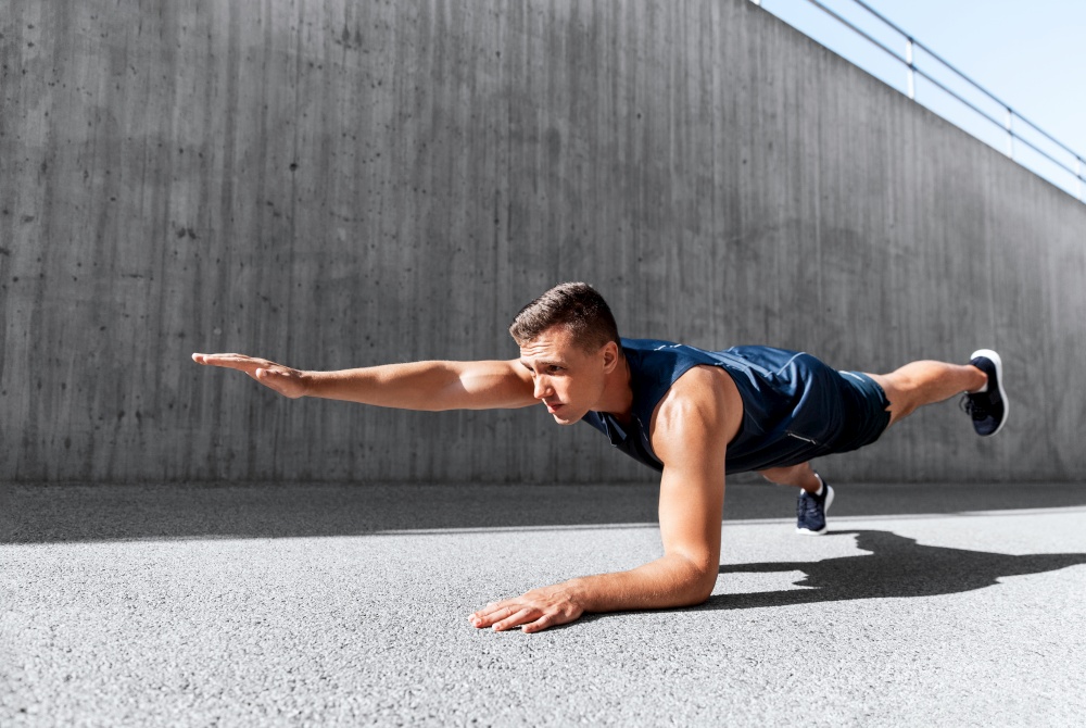 fitness, sport and training concept - young man doing plank on city street. young man doing plank on city street