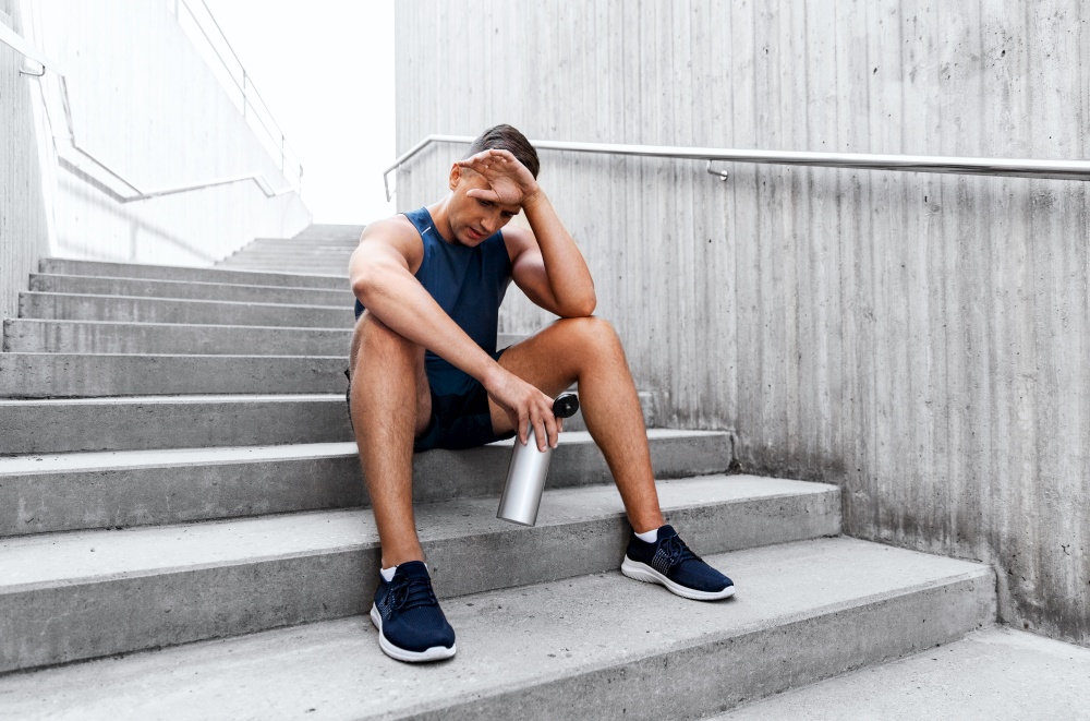 fitness, sport and people concept - tired young man with bottle of water sitting on stairs. tired sportsman with bottle sitting on stairs