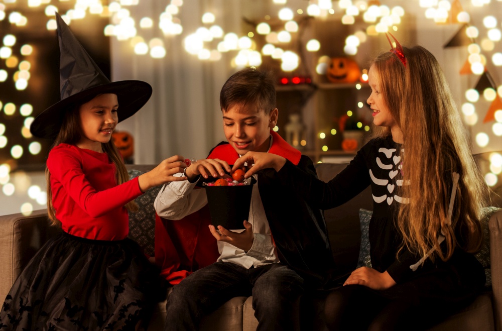 halloween, holiday and childhood concept - smiling boy and girls in costumes sharing candies at home. kids in halloween costumes sharing candies at home