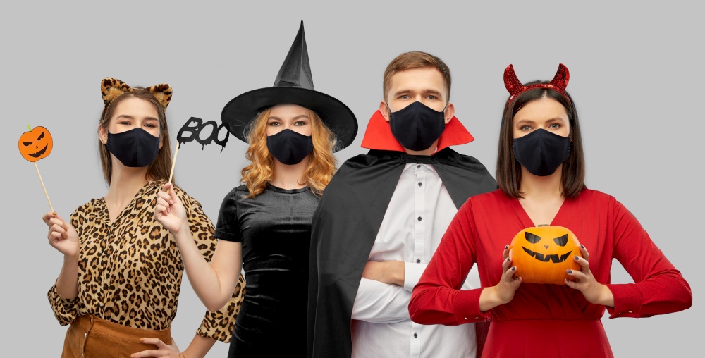 holiday, health and pandemic concept - friends in halloween costumes and black reusable masks over grey background. friends in halloween costumes and black masks