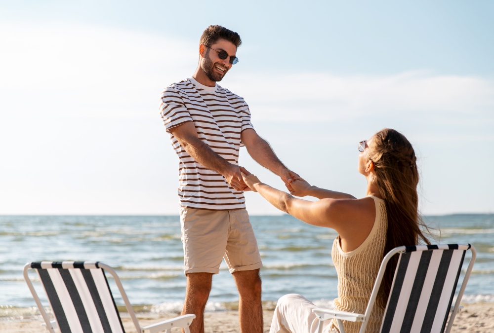 leisure, relationships and people concept - happy couple sitting in folding chairs and holding hands on summer beach. happy couple sitting in folding chairs on beach