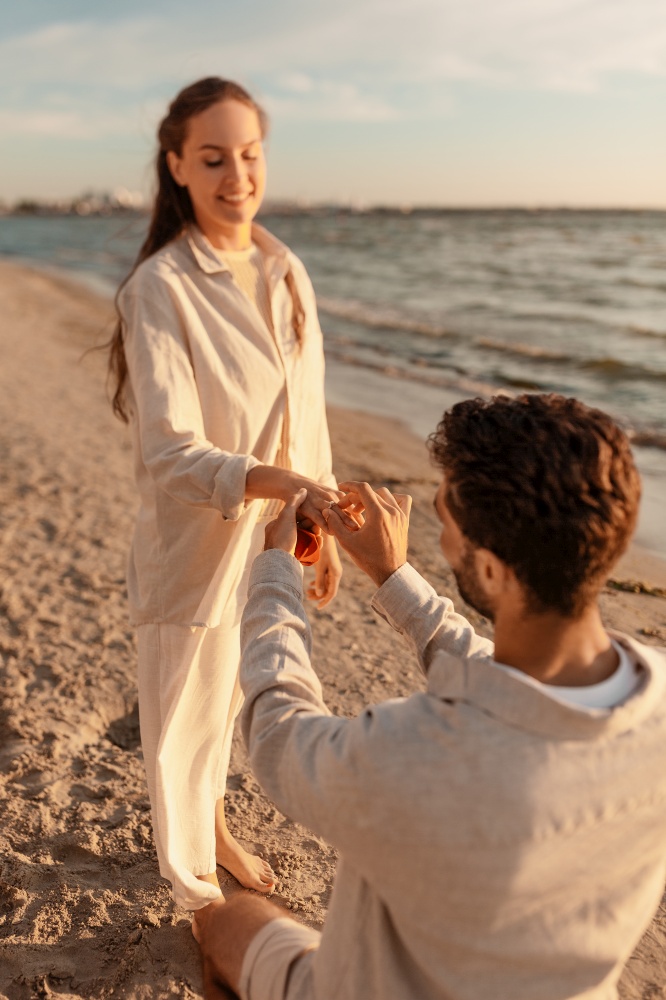 love and people concept - smiling young man with engagement ring making proposal to happy woman on beach. man with ring making proposal to woman on beach