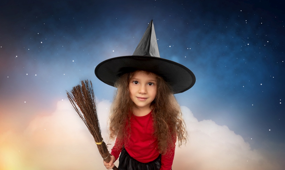 halloween, holiday and childhood concept - girl in costume and witch hat with broom over cloud and stars in night sky background. girl in witch hat with broom on halloween at night