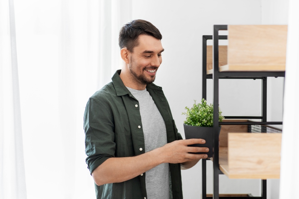 home improvement, decoration and people concept - happy smiling man placing flower in pot or houseplant to shelf. man decorating home with flower or houseplant