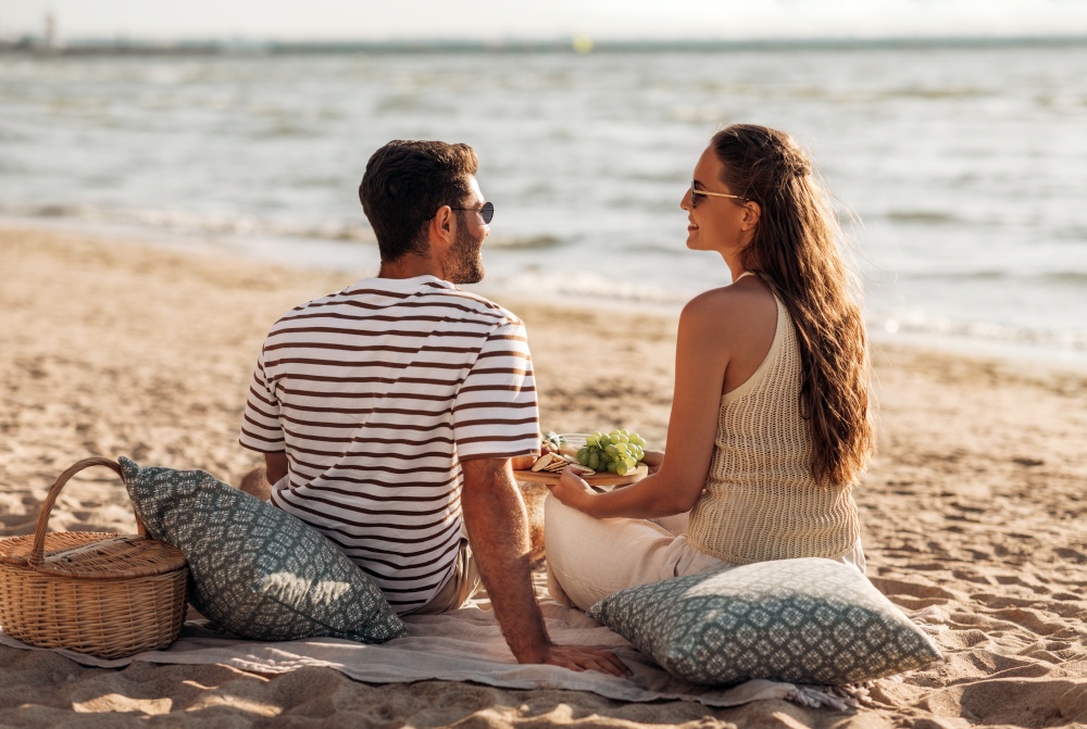 leisure, relationships and people concept - happy couple with food eating and having picnic on beach. happy couple with food having picnic on beach