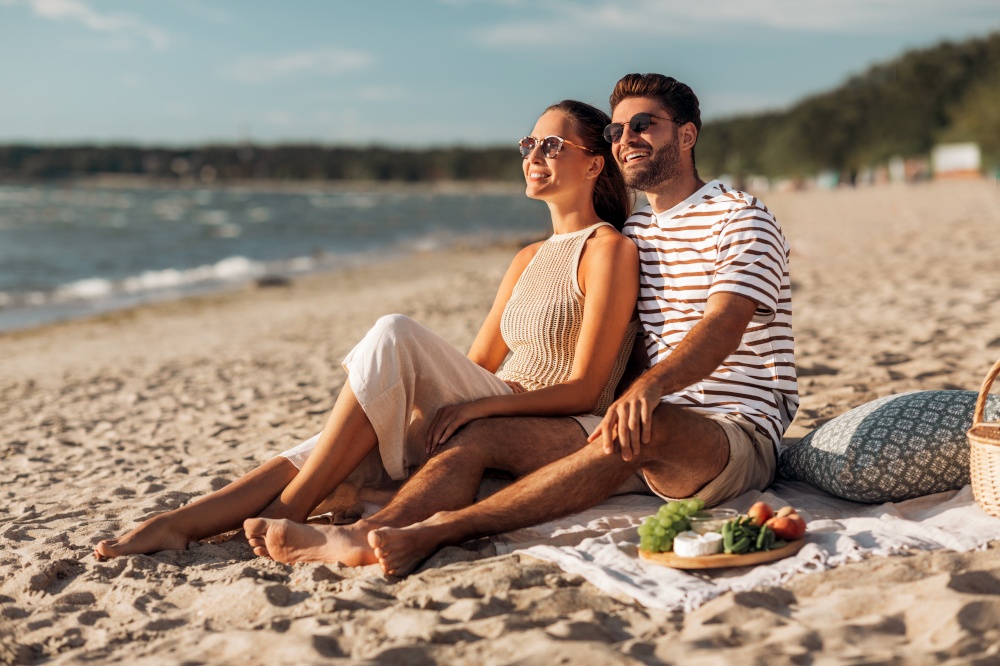leisure, relationships and people concept - happy couple having picnic on beach. happy couple with food having picnic on beach